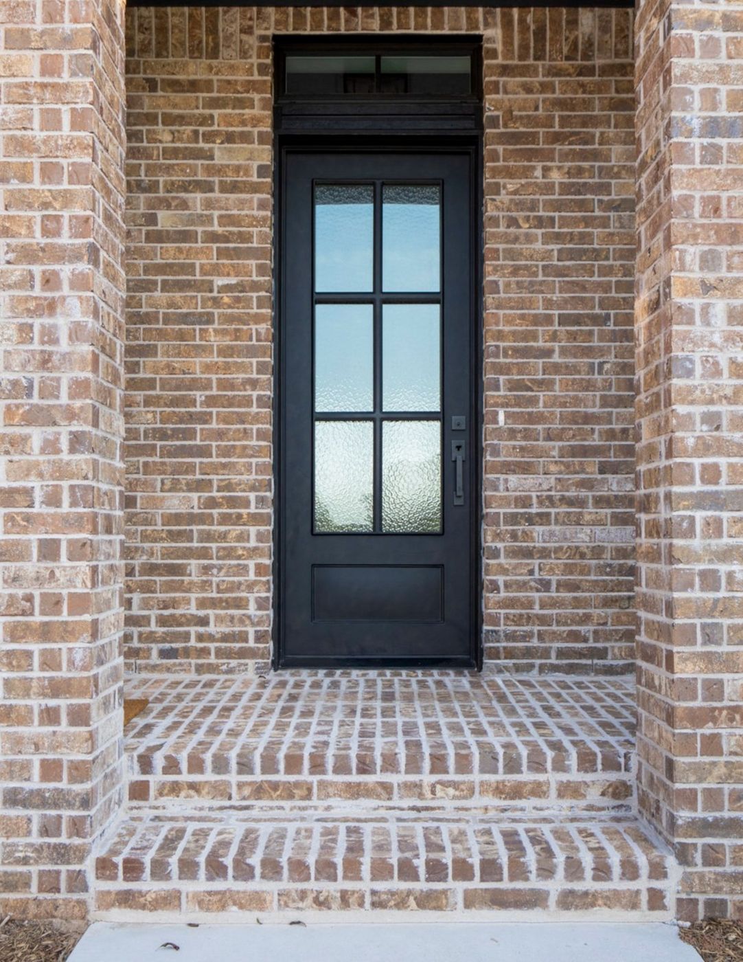 A black entry door with divided-lite glass set in a brick wall, fitted with a black handleset